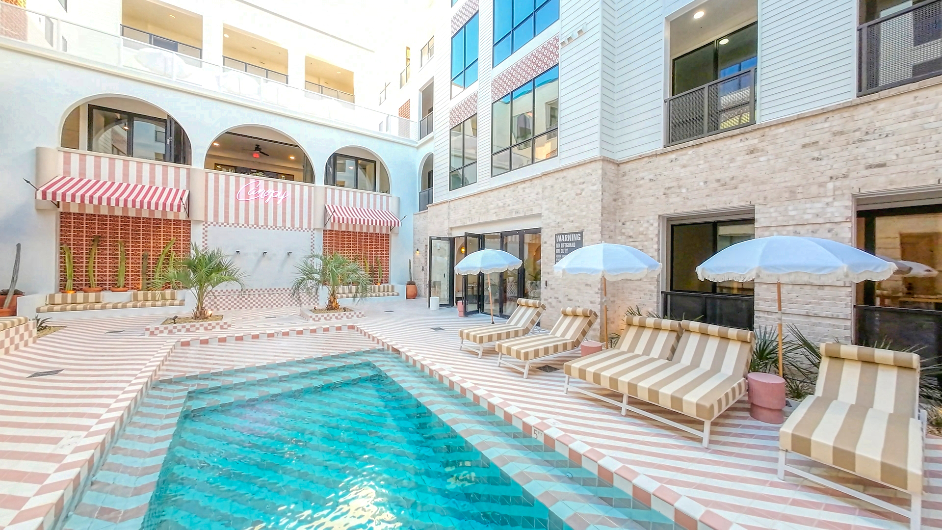 Resort-style pool at Bishop Canopy Apartments, with modern lounge chairs, clear blue water, and lush greenery.